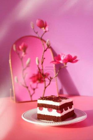 Photo for Chocolate cake with cherries. Piece of cake on a plate with fork. Bottle of pink vine reflected in arch mirror. Sweet dessert on pink background with magnolia blossoms. Slice of torte and Spring flowers . - Royalty Free Image