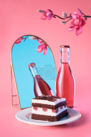 Photo for Chocolate cake with cherries. Piece of cake on a plate with fork. Bottle of pink vine reflected in arch mirror. Sweet dessert on pink background with plum blossoms. Slice of torte and Spring flowers . - Royalty Free Image