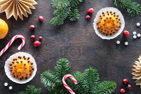 Photo for Wintertime dark background with pomander balls and cranberry. Classical decorations - tangerine with cloves. Handmade paper stars from brown baking paper, pine cones, fir twigs and stripy candy canes. - Royalty Free Image