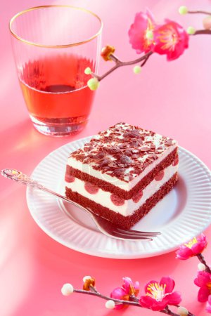 Téléchargez les photos : Gâteau au chocolat aux cerises acides. Pièce de gâteau sur une assiette avec fourchette. Dessert sucré sur fond rose avec des fleurs de prunes d'hiver, des décorations de fleurs roses. Verre de limonade rose ou vin de rose. - en image libre de droit