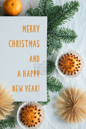 Photo for Fragrant pomander balls handmade from tangerines with cloves. Handmade paper stars from brown paper. Flat lay on off white textile and fir twigs. Text Merry Christmas and a Happy New Year on white canvas. - Royalty Free Image