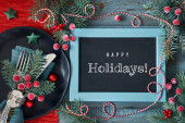 Christmas table setup with text Happy Holidays on blackboard, chalk board. Flat lay with Wintertime holiday decorations in green and red with frosted red berries and trinkets. Longsleeve T-shirt #625993828