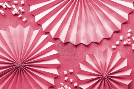 Foto de Pink paper fans and sweet marshmallows on pink textured background with paper fans. Flat lay, top view, monochromatic birthday or celebration background. - Imagen libre de derechos