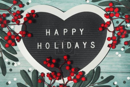 Photo for Text Happy Holidays on felt heart shape letter board, letterboard. Winter Christmas flat lay background with red rowan berry on mint green wood with snow sugar sprinkles. - Royalty Free Image