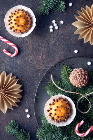 Photo for Wintertime dark background with fragrant pomander balls. Classical decorations - tangerine with cloves. Handmade paper stars from brown baking paper, pine cones, fir twigs and burning beewax candle. - Royalty Free Image