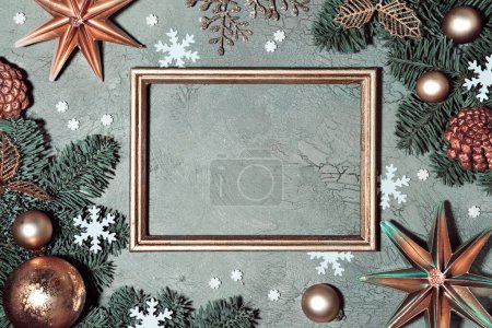 Photo for Christmas background. Flat lay with fir twigs decorated with red rowan berry, paper stars and snowflakes on grey green textured background. Copy-space, place for text in metallic copper frame. - Royalty Free Image