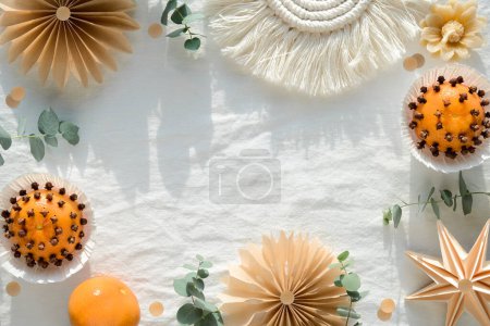 Photo for Fragrant pomander balls handmade from tangerines with cloves. Handmade paper stars from brown baking paper. Flat lay on off white textile tablecloth with eucalyptus. Wood Christmas tree toys, trinkets. - Royalty Free Image