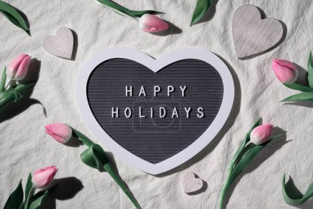 Spring flowers, decorated heart shape text board, textboard with caption Happy Holidays. Pink tulips and painted wooden hearts. Easter, springtime flat lay Birthday or Spring holiday background,