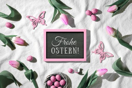 Photo for Easter background. Decorated background with blackboard. Text Frohe Ostern means Happy Easter in German language. Pink tulips, wood butterflies and quail eggs. Top view, flat lay, springtime decor. - Royalty Free Image