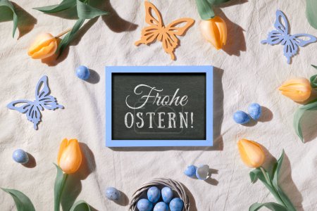 Photo for Easter background. Decorated background with blackboard. Text Frohe Ostern means Happy Easter in German language. Yellow tulips and quail eggs. Top view, flat lay, springtime decor. - Royalty Free Image