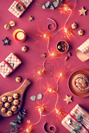 Téléchargez les photos : Viva Magenta couleur de l'année 2023. Fond rouge foncé de Noël. Pose plate monochromatique avec des bonbons de massepain, boîtes-cadeaux enveloppées, eucalyptus, noix, étoiles, bougie et guirlande électrique. - en image libre de droit