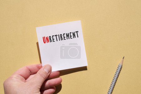 Photo for Unretirement word written on square paper note in hand. Top view, flat lay on yellow paper background with pencil. - Royalty Free Image