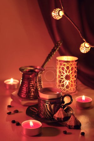 Photo for Turkish coffee pot and traditional cup with oriental sweets. Metal lantern, ornate garland and tea lights. Viva magenta, color of the year 2023. Red purple background lit by candlelight. - Royalty Free Image