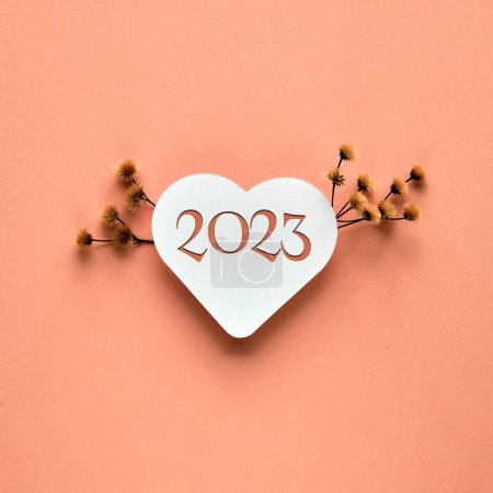 2023 happy new year. Paper heart with number 2023. Dry pampas grass, flowers, floral decorations on orange paper. Minimalistic square composition.