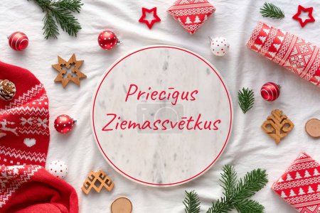 Foto de Priecigus Ziemassvetkus significa Feliz Navidad en letón. Patrones bálticos etnográficos de Letonia, baratijas de madera, papel de regalo, cajas de regalo con ramitas de abeto sobre fondo textil blanco. - Imagen libre de derechos