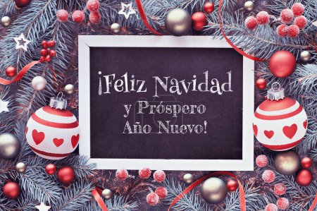 Photo for Christmas frame in green and red, top view, flat lay. Fir twig decorated with baubles, berries and Xmas stars. Feliz Navidad means Merry Christmas in Spanish language. - Royalty Free Image