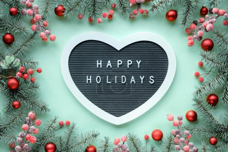 Photo for Christmas heart shaped text board, message greeting words Merry Christmas. Frame with fir twigs, berries and red baubles. Top view, flat lay, festive Xmas background on mint green paper background. - Royalty Free Image