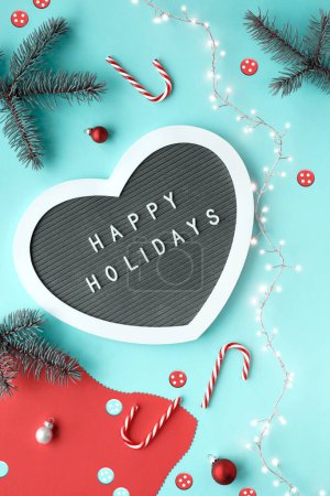 Photo for Christmas heart shaped text board, message greeting words Merry Christmas. Flat lay with fir twigs, candy canes, red baubles. Top view, festive Xmas background on mint blue paper background. - Royalty Free Image