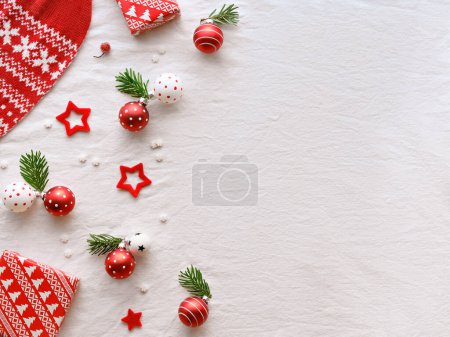 Photo for Decorative border with winter decor. Decorative scarf, knitted sweater with wihite winter ornaments. Red baubles with fir twigs, gift box and red felt stars. Red decor on off white textile, copy-space. - Royalty Free Image
