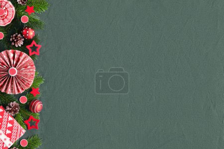 Téléchargez les photos : Bordure décorative pour décor d'hiver ethnique balte. Noël, festival d'hiver letton. Guirlande décorative avec brindilles de sapin, coffrets cadeaux, éventails en papier, étoiles en feutre rouge. Décor rouge sur textile lin vert foncé. - en image libre de droit