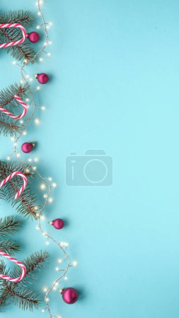 Téléchargez les photos : Guirlande de Noël, bordure, bannière avec brindilles de sapin, cannes à bonbons, guirlande et babioles rouges. Vue de dessus, plan plat, fond de Noël festif sur bleu menthe. Fond d'écran pour les histoires de médias sociaux avec copie-espace. - en image libre de droit