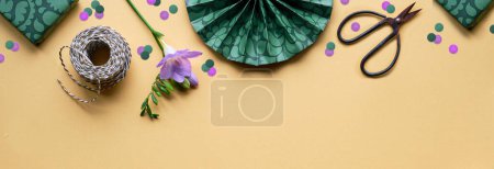 Téléchargez les photos : Spring flowers and gift boxes. Golden yellow paper background with green presents, scissors, cord. Flat lay, top view with purple freesia. Narrow orange green banner, panoramic element for web design. - en image libre de droit