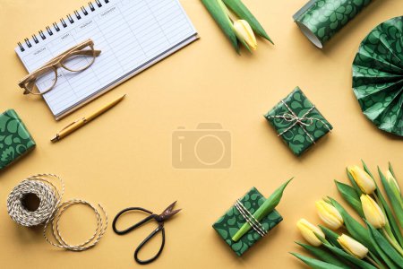 Foto de Weekly planner, female desktop. Spring freesia, tulip flowers and gift boxes. Orange background with green wrapping paper, scissors and cord. Flat lay, top view. Yellow, green, purple pastel colors. - Imagen libre de derechos