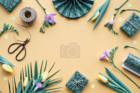 Foto de Spring freesia and tulip flowers and gift boxes. Golden yellow background with green wrapping paper, scissors and cord. Flat lay, top view with copy-space. Orange, green, purple pastel colors. - Imagen libre de derechos