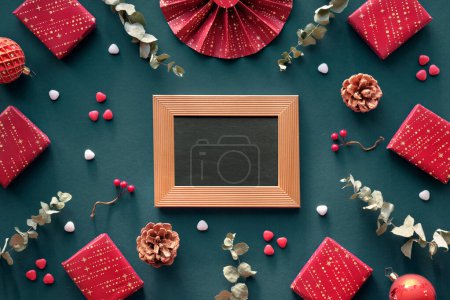 Foto de Christmas gift boxes, flat lay in dark green and red colors. Wellness presents - gua sha stone, cream, essence serum, oil bottle. Cyan background with dry eucalyptus, copy-space, place on blackboard. - Imagen libre de derechos