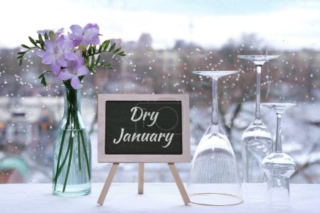 Photo for Dry January, month without alcohol. Text Dry January on blackboard, chalk board. Empty vine and beer drinking glasses, freesia flowers. Window with raindrops, grey winter city skyline on background. - Royalty Free Image