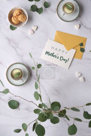 Téléchargez les photos : Happy Mother's day background. Mint green postal envelope, white card, pen and office stationary. Eucalyptus twigs on stone, overhead view. Delicate grey green silver dollar eucalyptus leaves. - en image libre de droit