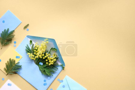 Téléchargez les photos : Spring banner. Fresh mimosa flowers in blue paper envelope . Geometric flat lay, top view with flowers and greeting cards on yellow background, copy-space. Springtime greeting design. - en image libre de droit
