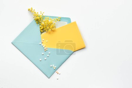 Téléchargez les photos : Fresh mimosa flowers in blue paper envelope with yellow card, flat lay, top view on pale yellow background. Springtime greeting mockup. Birthday, spring invitation, March 8 International Women's Day. - en image libre de droit