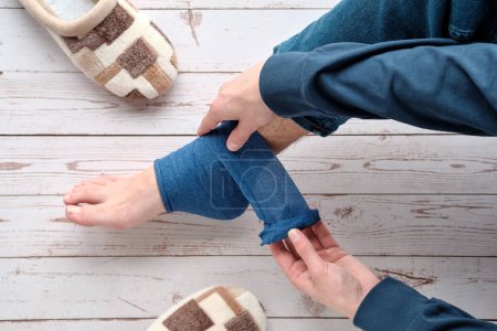 Téléchargez les photos : Teenage boy wrapping compression bandage around sprained ankle to reduce ache. Crutches on the floor. Feet trauma, injury. Medical Ankle Bandage. Ankle Medical Support Strap, Adjustable Wrap Bandage. - en image libre de droit