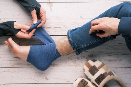 Foto de An adult wrapping compression bandage around sprained ankle of teenage boy to reduce ache. Feet trauma, injury. Medical Ankle Bandage. Ankle Medical Support Strap, Adjustable Wrap Bandage. - Imagen libre de derechos