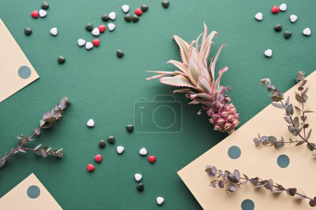 Téléchargez les photos : Ananas, brindilles d'eucalyptus dans une couche plate sur le livre vert Avec bonbons en forme de coeur, décor naturel à faible impact - en image libre de droit