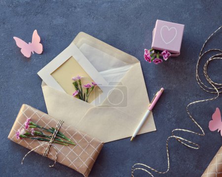 Téléchargez les photos : Enveloppe et concept de carte de vœux faite par soi-même avec des fleurs d'oeillet fraîches. Cadeau enveloppé, carte postale en papier, enveloppe en papier, cordon, ciseaux et œillets violets. - en image libre de droit