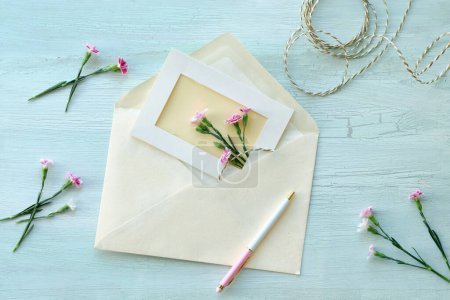 Téléchargez les photos : Enveloppe et concept de carte de vœux faite par soi-même avec des fleurs d'oeillet fraîches. Cadeau enveloppé, carte postale en papier, enveloppe en papier, cordon, ciseaux et œillets violets. - en image libre de droit