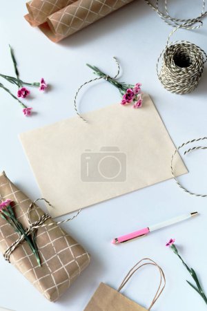 Téléchargez les photos : Concept de carte de vœux avec enveloppe et fleurs d'oeillet. Carte postale en papier vierge, enveloppe en papier artisanal, cordon, ciseaux et œillets violets. Carte blanche vierge pour maquette. - en image libre de droit