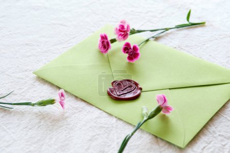 Photo for Envelope wax seal with carnation flowers on white table. Self made low impact greeting card. - Royalty Free Image