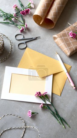 Téléchargez les photos : Concept de carte de vœux avec enveloppe et fleurs d'oeillet. Carte postale en papier vierge, enveloppe en papier artisanal, cordon et ciseaux. Carte blanche vierge pour la maquette. Copiez l'espace pour votre texte d'accueil. - en image libre de droit