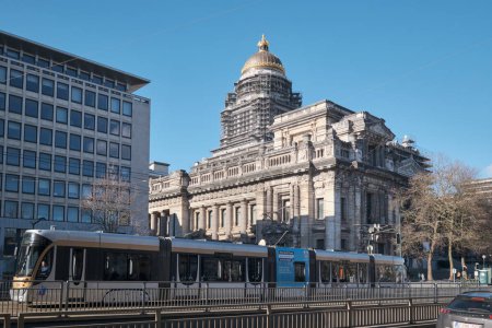 Foto de BRUSELAS, BÉLGICA - 26 DE FBERUARIO DE 2023: Un tranvía en las vías frente al Palacio de Justicia, un gran edificio abandonado en Bruselas, Bélgica. - Imagen libre de derechos