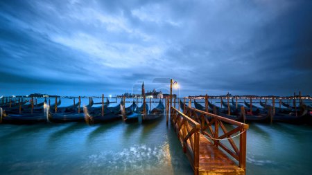 Téléchargez les photos : Italie, gondoles amarrées par Venice Embankment la nuit. Lumière solitaire sur jetée en bois humide. - en image libre de droit