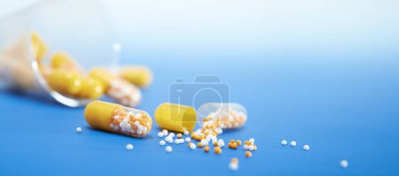 Photo for Pills spilling out of a bottle on a blue surface. Copyspace, place for text. - Royalty Free Image