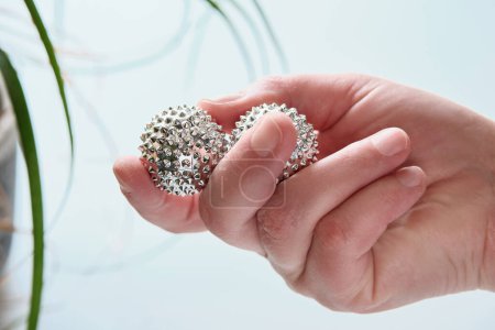 Foto de Bolas magnéticas de metal plateado en mano femenina. Herramienta puntiaguda para masaje de manos. Primer plano en la mano de mediana edad. - Imagen libre de derechos