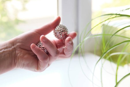 Foto de Bolas magnéticas de metal plateado en mano femenina. Herramienta puntiaguda para masaje de manos. - Imagen libre de derechos