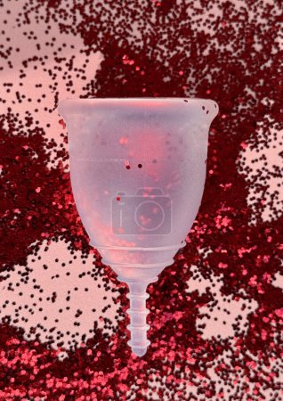 Foto de Primer plano de una copa menstrual sobre fondo de purpurina roja, ginecología e higiene, cero residuos sostenibles para tampones desechables. - Imagen libre de derechos