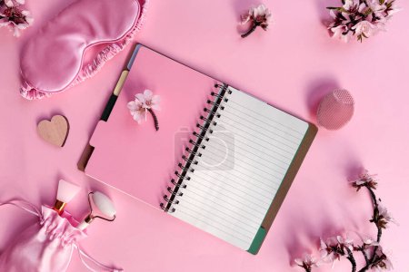 Photo for Square pink overhead background, quality of sleep, and self care routine. Sleeping mask, blank notebook with copy-space, massage stone roller, cream and wooden heart on pink paper. - Royalty Free Image