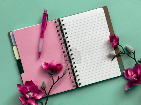 Foto de Un cuaderno rosa con un bolígrafo colocado encima, listo para escribir. Flores de magnolia rosa. - Imagen libre de derechos