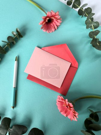 Photo for A pink envelope, a pen, and pink gerbera flowers arranged on a vibrant turquoise background. Copy-space on greeting card. - Royalty Free Image
